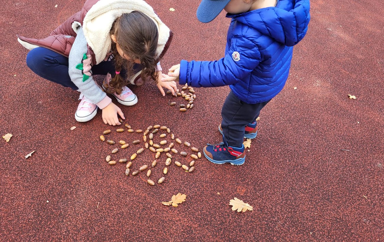 Two children arranging acorns into a pattern outdoors