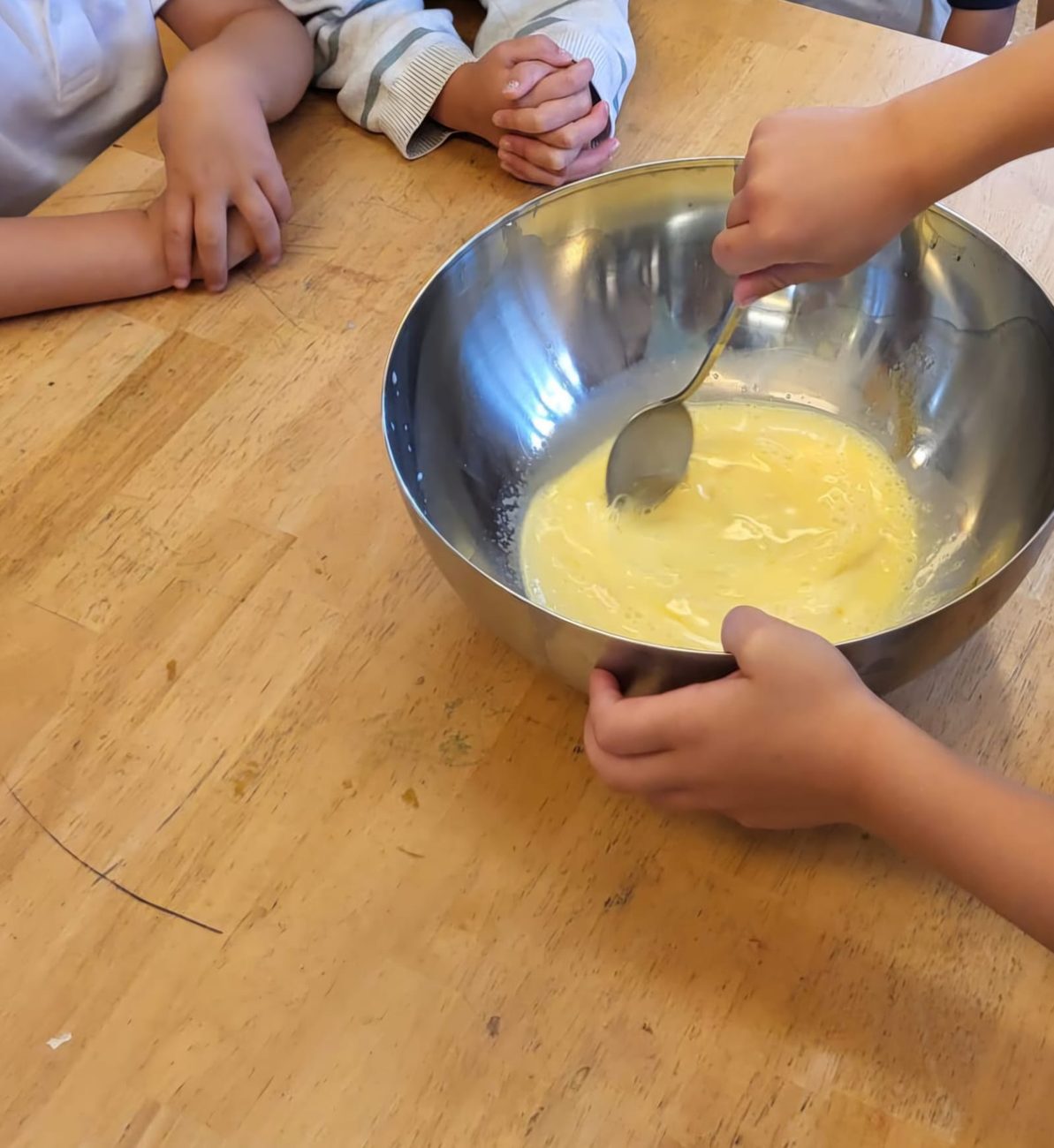 Three children at a wooden table with a mixing bowl