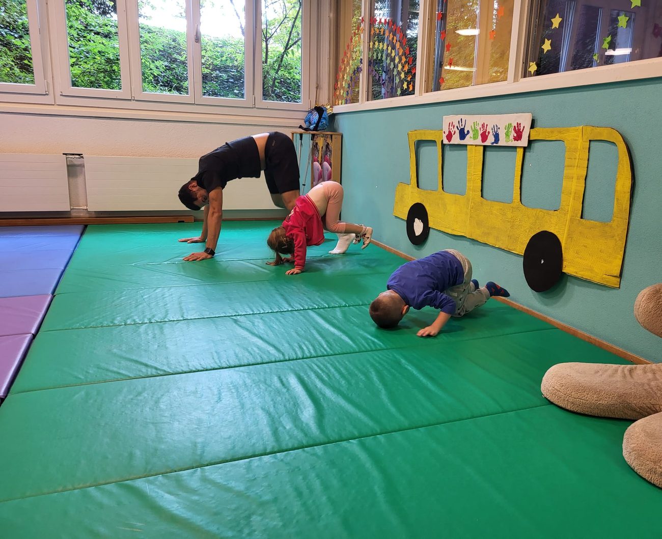 Children in yoga poses on green mats next to a painted yellow bus on the wall