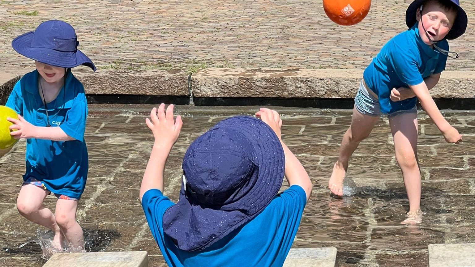 Children playing with a ball in the fountain on a sunny day